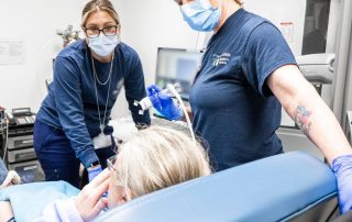 Two respiratory caregivers provide a breathing treatment to a patient in a hospital room.