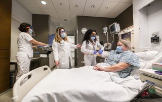 Cleveland Clinic nurses and staff wearing masks provide care to a patient in a hospital bed, with medical monitors and equipment in the room