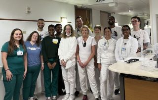 A group of Cleveland Clinic caregivers, wearing scrubs and white coats, stand together smiling in the Transplant Special Care Unit.