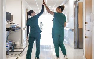 Two Cleveland Clinic nurses in green scrubs share a high-five while walking down a hospital hallway.