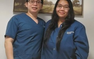 Two Cleveland Clinic pharmacy staff members, Darius and Ela, wearing blue scrubs and jackets stand side by side, smiling at the camera.