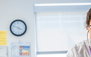 Smiling nurse using a stethoscope while caring for a patient in a hospital room.