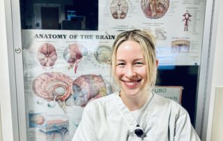 Sara wearing a Cleveland Clinic scrub top stands in front of a wall poster detailing brain anatomy.