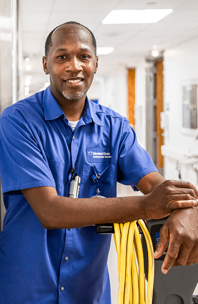 A smiling male EVS Technician leaning on a floor buffer in a hospital setting