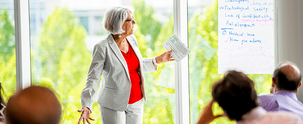 A female instructor at a white board conducting a training class in front of a group of professionals in a conference room